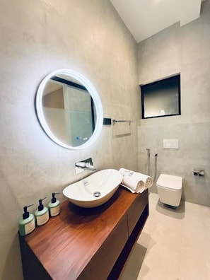 Un baño moderno con un tocador de madera, un espejo redondo, un lavamanos blanco y un inodoro.