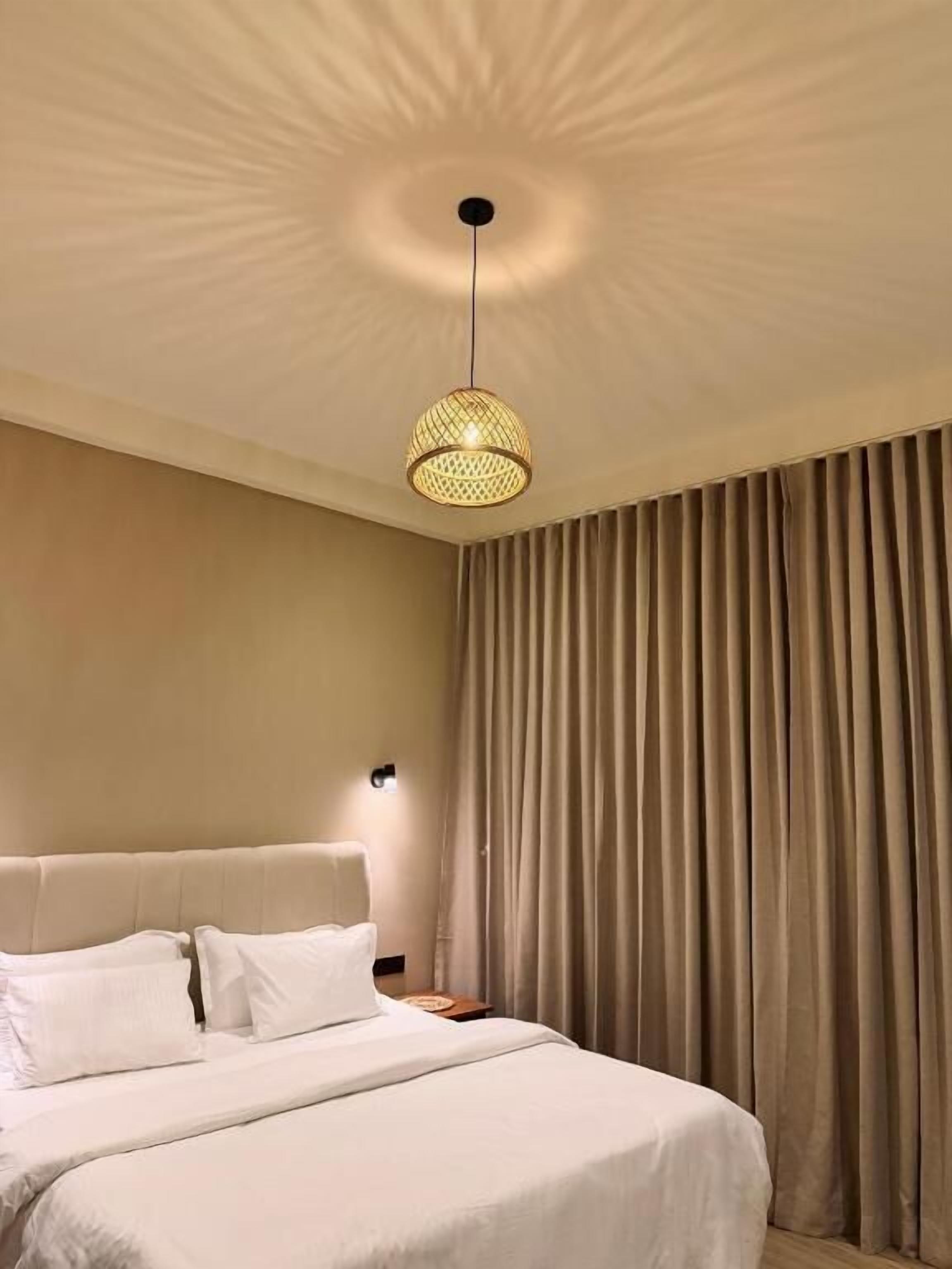 Una habitación de hotel con una cama grande, cabecera, luz de pared y cortina.