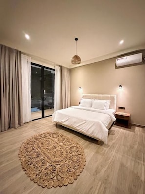 Un dormitorio moderno con una cama grande, un tapete decorativo redondo y un ventanal corredero que da a un balcón.