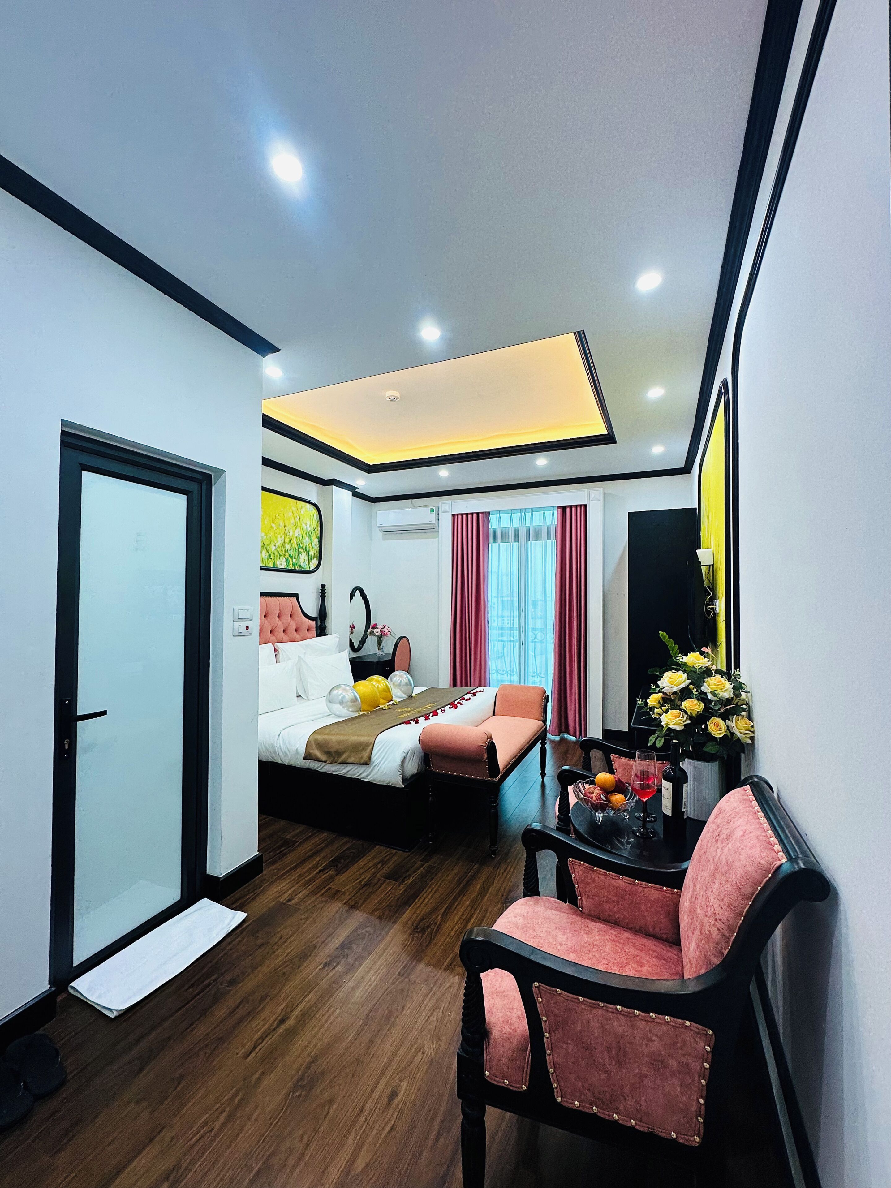 A hotel room with a bed, a desk with a chair, a mirror, and a window with curtains.