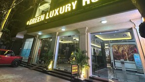 L'ingresso di un hotel con un cartello che riporta 'GREEN LUXURY HOTEL', una facciata in vetro e un'auto rossa parcheggiata all'esterno.