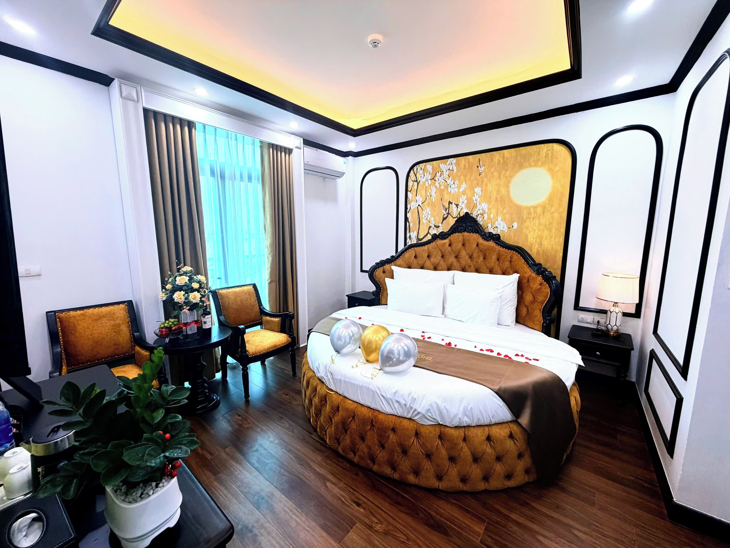A hotel room with a large bed, a chair, a small table with a plant, and a window with curtains.