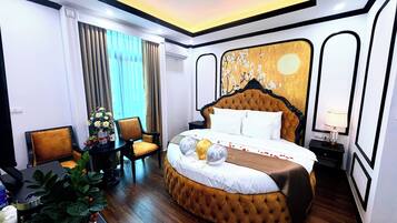 A hotel room with a large bed, a chair, a small table with a plant, and a window with curtains.