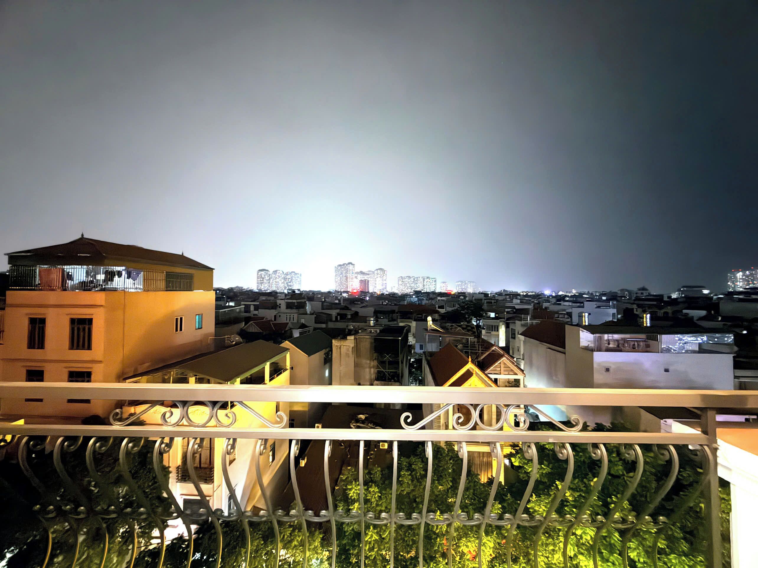 A cityscape at night with buildings and a balcony with ornate metal railings.