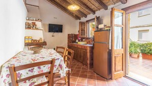 A compact kitchen with wooden cabinets, a dining table with a floral tablecloth, and a large refrigerator. - Domm'e Antoni - Apartment in the heart of Ogliastra in stone and juniper (Baunei)