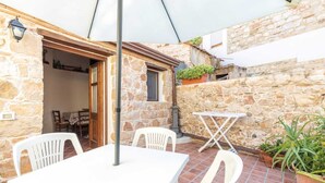 A stone-walled outdoor patio with a table and chairs, a small window, and potted plants. - Domm'e Antoni - Apartment in the heart of Ogliastra in stone and juniper (Baunei)