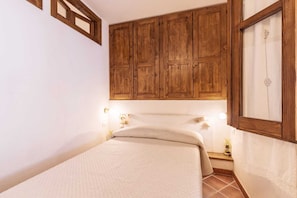 A bedroom with a wooden headboard, a bed with a quilted cover, and a nightstand with a lamp. - Domm'e Antoni - Apartment in the heart of Ogliastra in stone and juniper (Baunei)