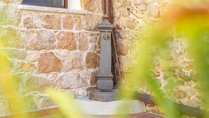 A stone wall with a metal structure, possibly a water spout, and a tiled floor. - Domm'e Antoni - Apartment in the heart of Ogliastra in stone and juniper (Baunei)