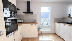 A modern kitchen with a built-in oven, a black range hood, and a window overlooking a cityscape. - Élégant 1 Chambre à Montparnasse (Paris)