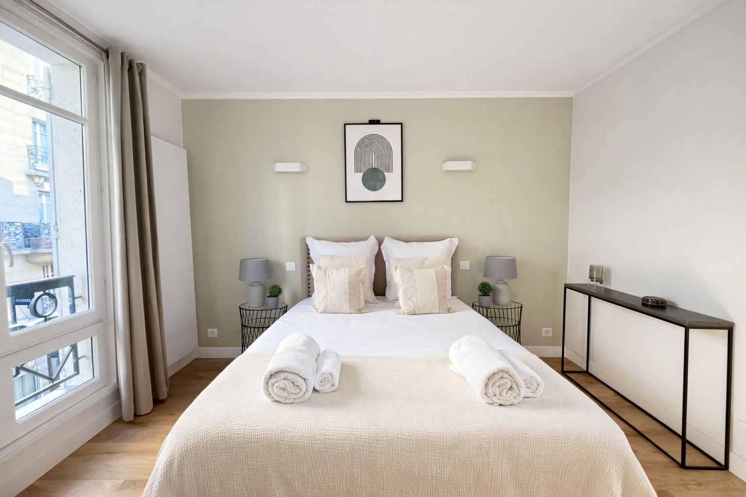 A hotel room with a large bed, two bedside tables with lamps, a framed picture on the wall, and a view of the city through the window.