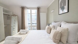 A hotel room with a large bed, a wardrobe, a window with curtains, and a framed picture on the wall. - Élégant 1 Chambre à Montparnasse (Paris)