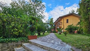 A pathway leading to a building with a stone staircase, surrounded by greenery and a clear sky.