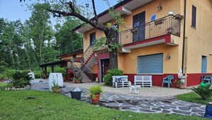 A two-story building with a red and yellow facade, a visible staircase, and a paved courtyard with potted plants and outdoor furniture.