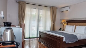 Hotelkamer met een houten bed, een bureau met waterkoker, een lamp en uitzicht door de gordijnen.