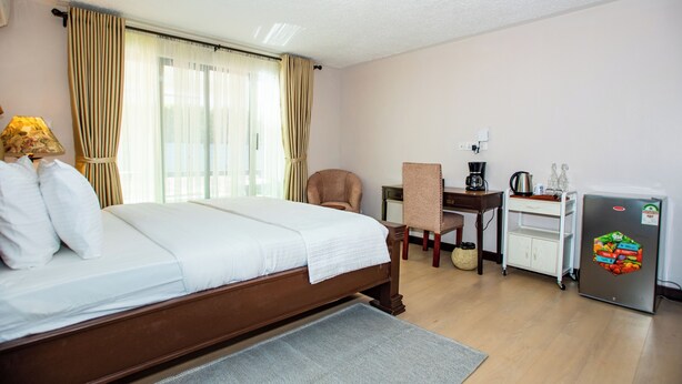 Een hotelkamer met een bed, een bureau, een stoel, een koelkast en een raam met gordijnen.