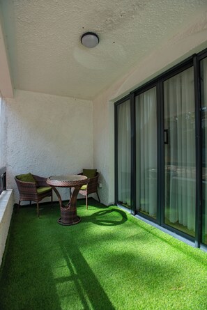 Un balcón con césped artificial, mobiliario de mimbre y una puerta de cristal.