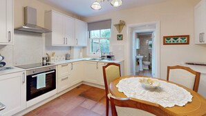 Una cocina moderna con muebles blancos, horno empotrado y comedor con mesa para dos.