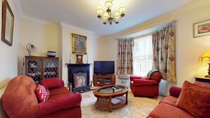 Un salón con sofás rojos, televisor, chimenea y candelabro.