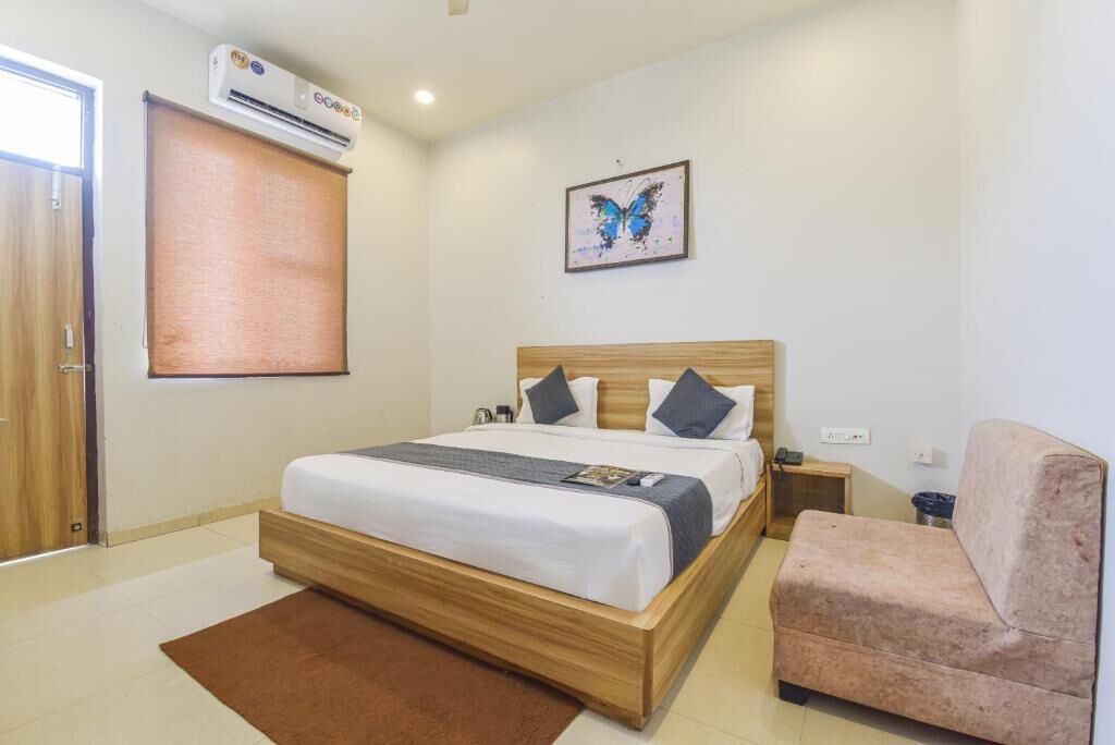 Ein Schlafzimmer mit einem hölzernen Bett, einem braunen Teppich, einem pinkfarbenen Sessel, einer wandmontierten Klimaanlage und einem Bilderrahmen mit einem Schmetterlingsmotiv.