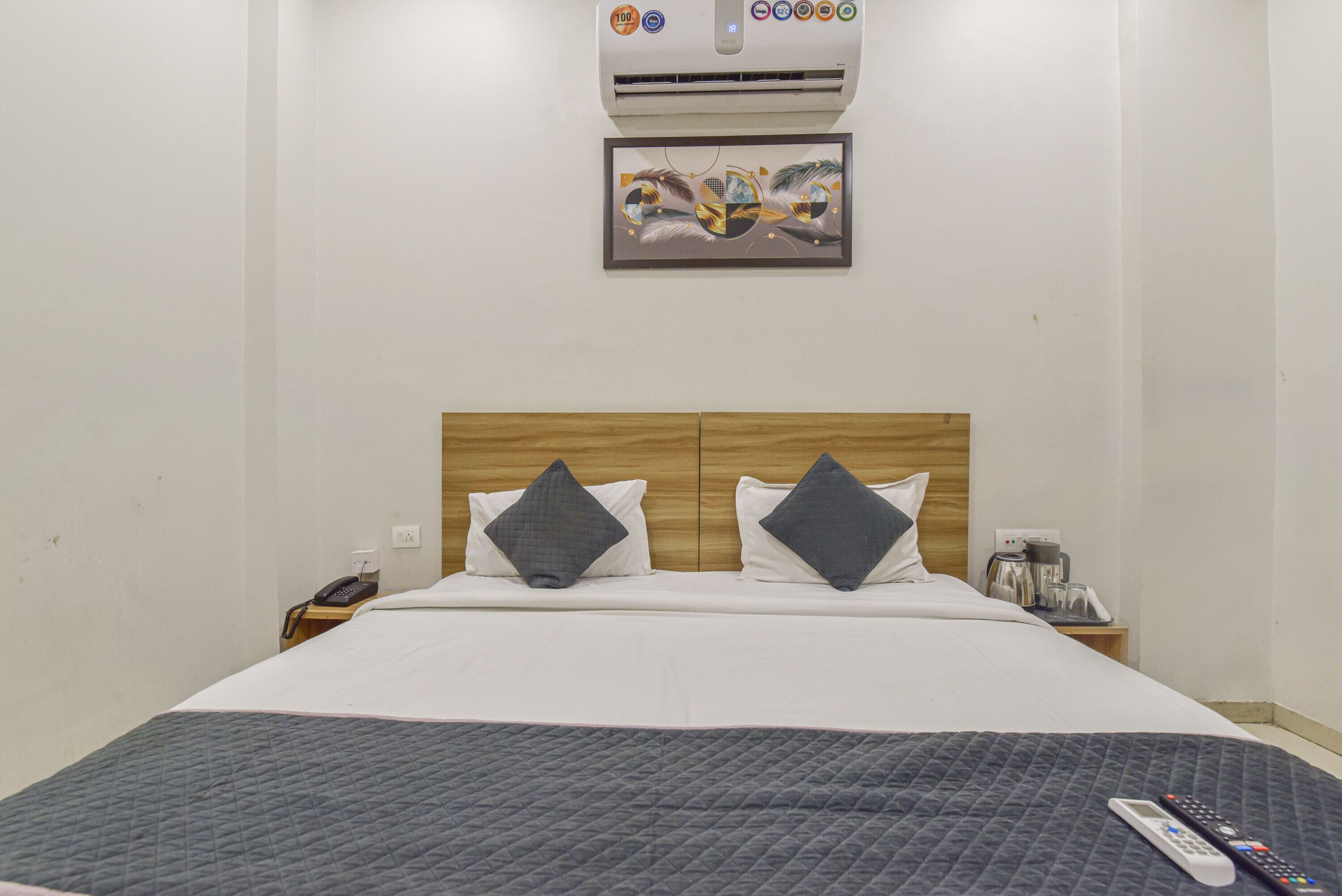 A hotel room with a large bed, two pillows, a bedside table with a phone, and a wall-mounted air conditioner.