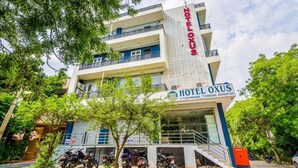 Un hôtel à plusieurs étages, appelé Hôtel Oxus, qui se distingue par son enseigne bien visible, ses balcons et les motos garées devant.