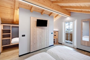 Ein Schlafzimmer mit Holzboden, einem an der Wand montierten Fernseher, einer Schiebetür zu einem Balkon und Einbauschränken.