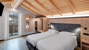 Et soveværelse med to senge, træbjælker i loftet, et stort vindue og en skydedør til en balkon.