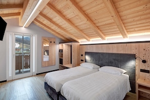 Ein Schlafzimmer mit zwei Betten, Holzbalkendecke, einem großen Fenster und einer Schiebetür zu einem Balkon.