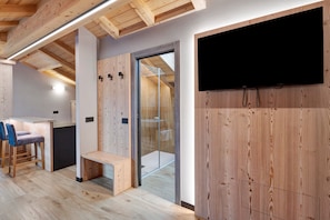 Ein modernes Interieur mit Holzvertäfelung, einem flachbildfernseher an der Wand, einer Bank und einem kleinen Tisch mit Stühlen.