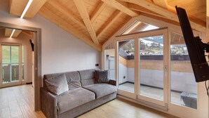 A modern loft-style room with a wooden ceiling, a gray sofa, and large sliding glass doors leading to an outdoor area. - Apartment '4 Bilocale Est' with Private Terrace (Livigno)