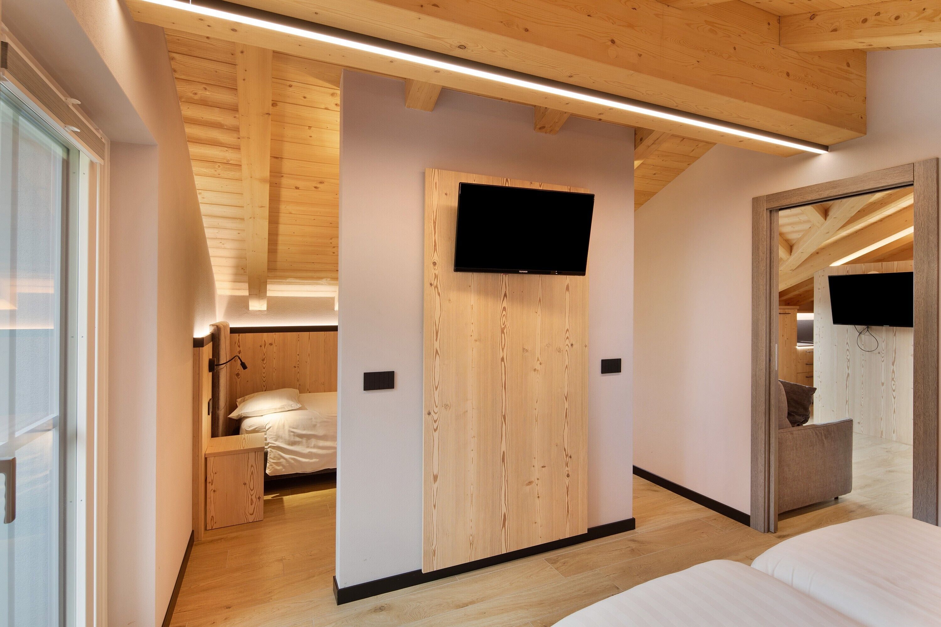 Ein modernes Hotelzimmer mit Holzvertäfelung, einem Flachbildfernseher, einem Bett und einer kleinen Sitzecke.