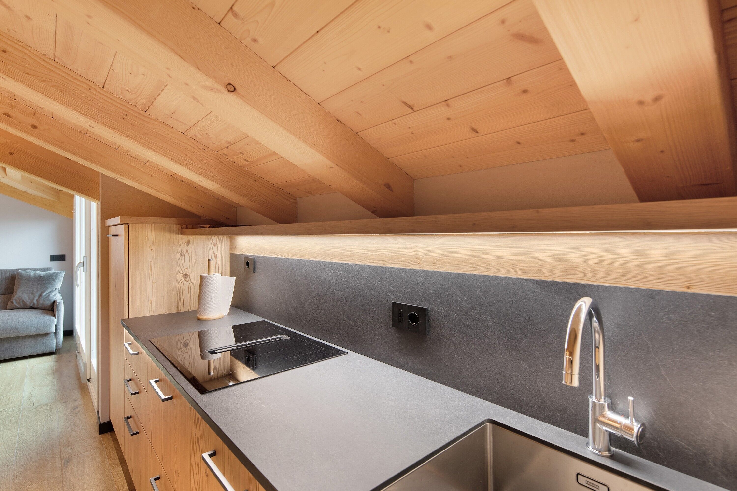 A modern kitchen with wooden beams, a black countertop, a stainless steel sink, and a built-in stove.