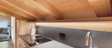 A modern kitchen with wooden beams, a black countertop, a stainless steel sink, and a built-in stove.