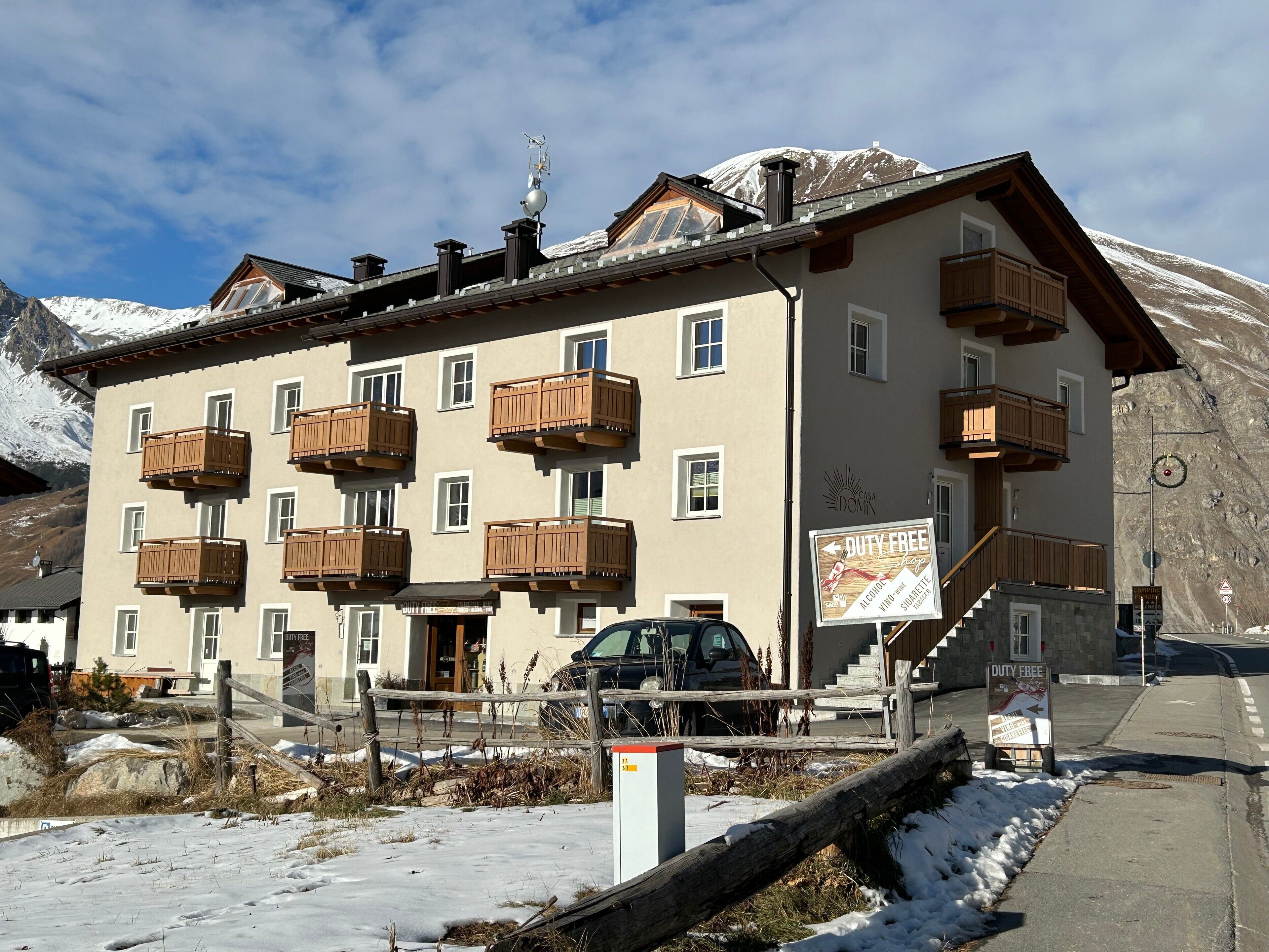 A multi-story building with wooden balconies, a sign indicating duty-free alcohol, and a mountain backdrop.