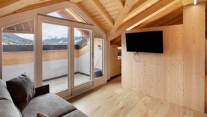 A modern loft bedroom with a wooden ceiling, a large sliding glass door to a balcony, a flat-screen TV mounted on the wall, and a grey sofa. - Apartment '4 Bilocale Est' with Private Terrace (Livigno)