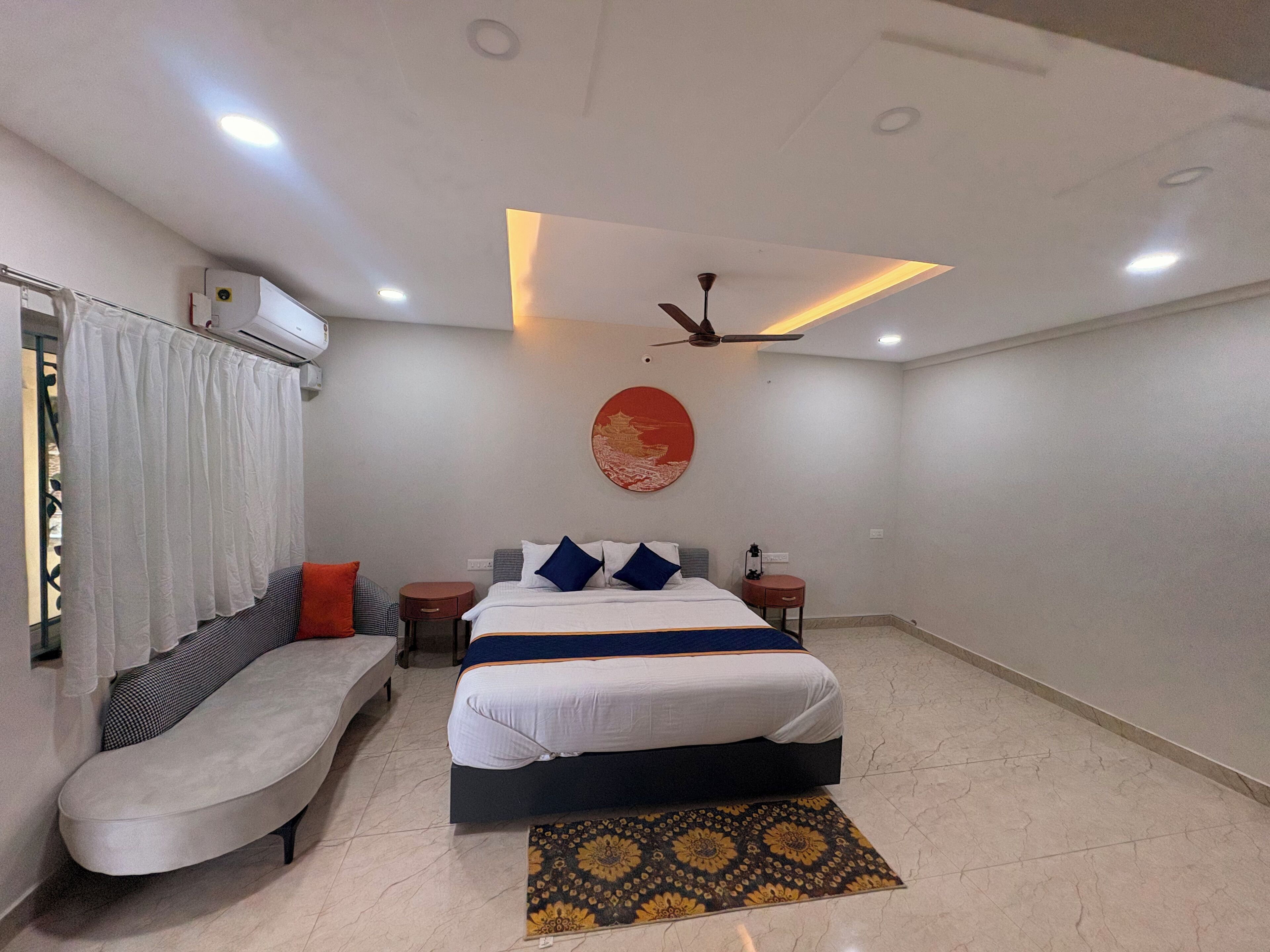 A modern bedroom with a bed, a sofa, a ceiling fan, and an air conditioning unit.