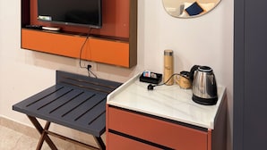 Une chambre d’hôtel avec un téléviseur fixé au mur, une petite table avec une bouilloire, une tasse et une boîte, et un miroir sur le mur.