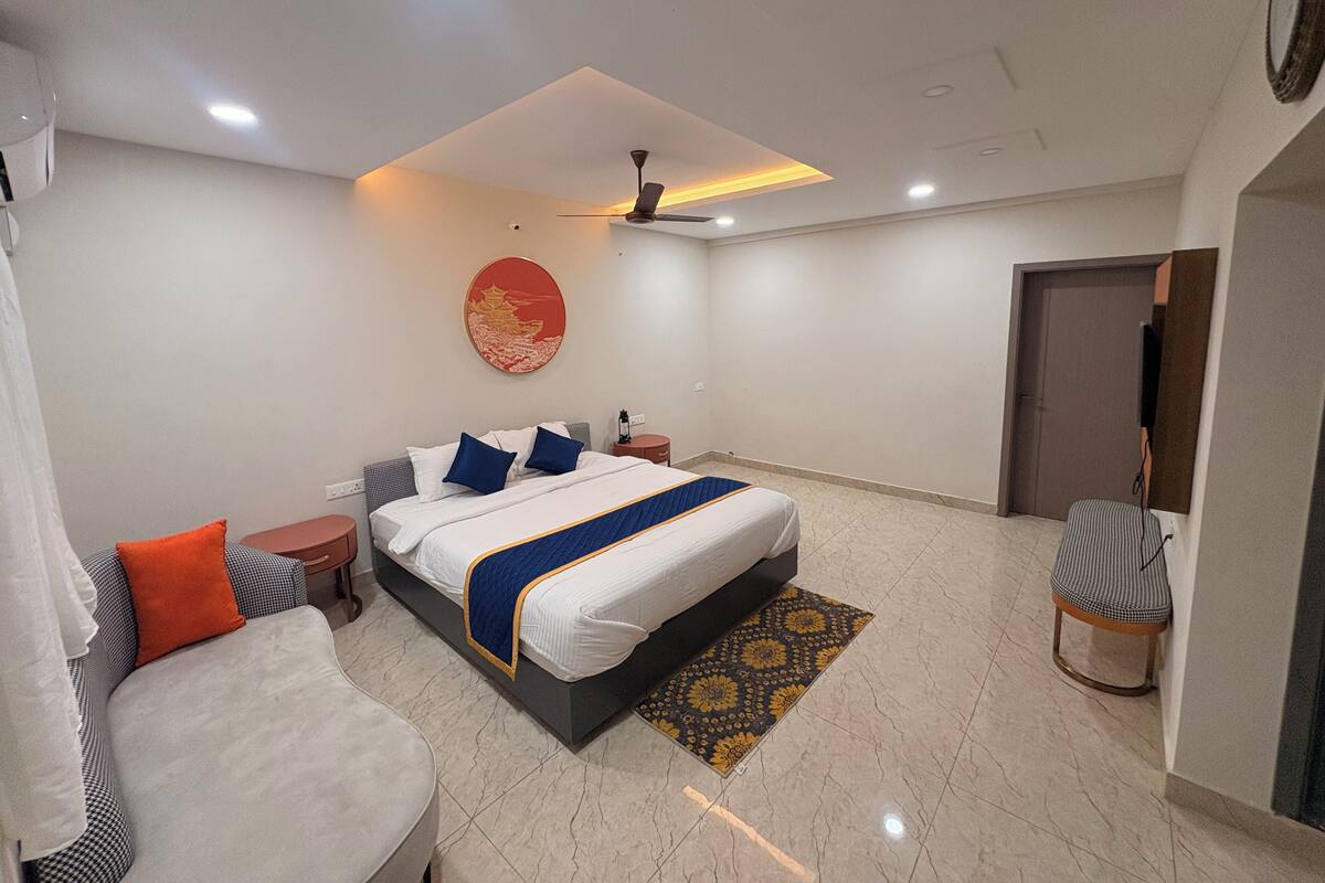 Una habitación de hotel moderna con cama, mesitas de noche, una silla, ventilador de techo y una puerta.