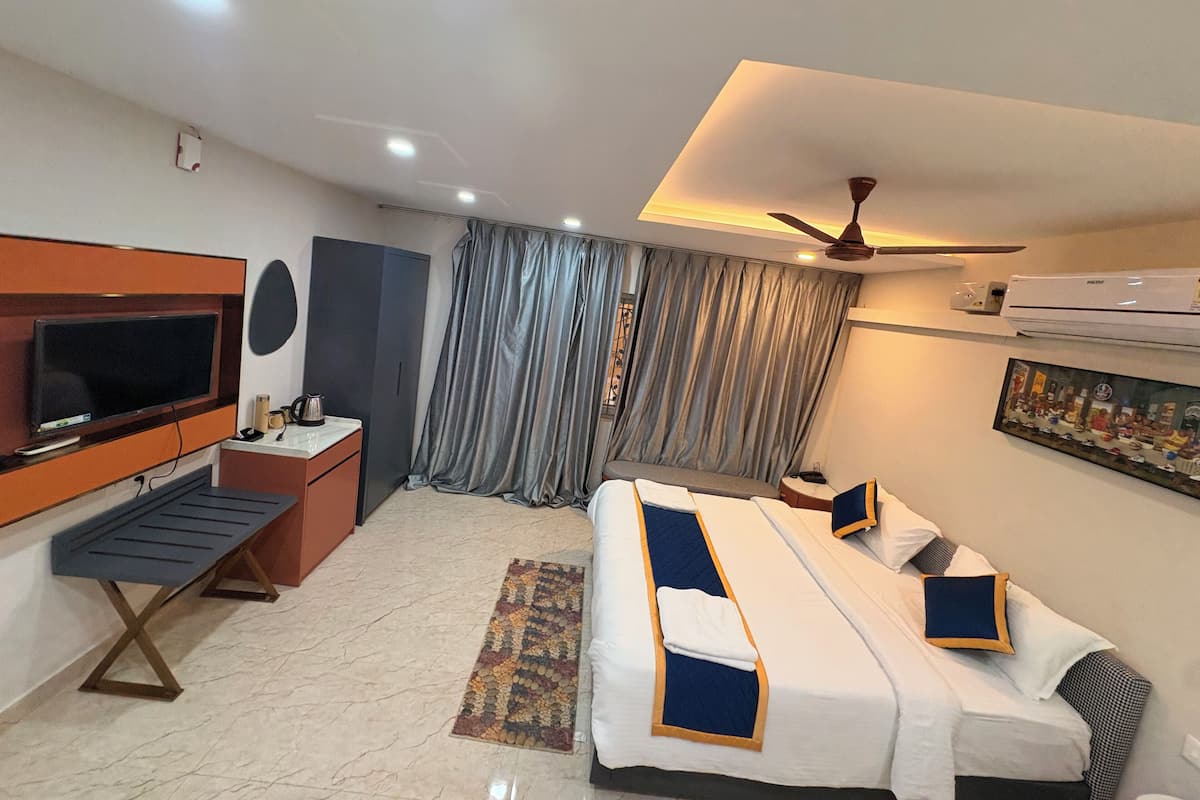 Una habitación de hotel con televisión, cama, escritorio, silla, ventilador de techo y aire acondicionado.