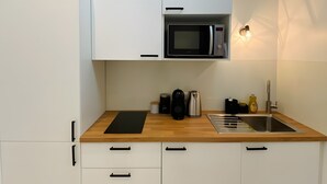 A compact kitchen with white cabinets, a microwave, a kettle, a sink, and a wooden countertop.