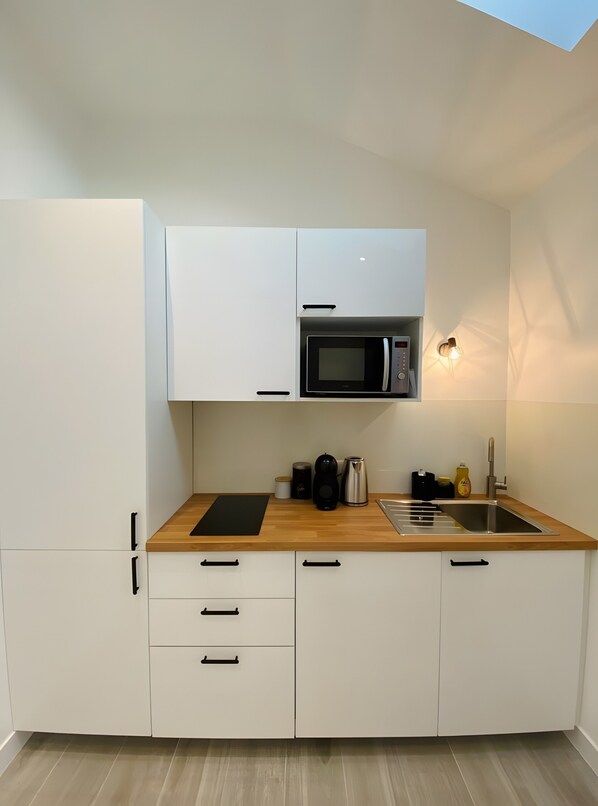 A compact kitchen with white cabinets, a microwave, a kettle, a sink, and a wooden countertop.
