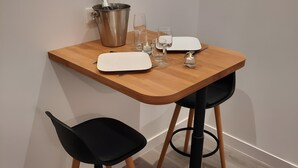 A small dining area with a wooden table, two black chairs, a white placemat, a metal bucket, and a wine glass.