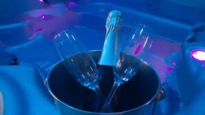 A metal bucket with a bottle and glasses on a reflective surface, possibly a poolside area.
