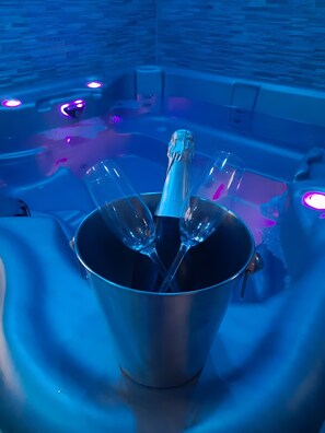 A metal bucket with a bottle and glasses on a reflective surface, possibly a poolside area.
