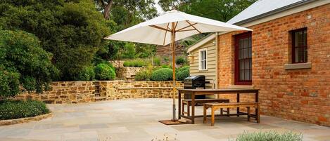 A patio with a table and chairs, a barbecue grill, and a large umbrella.