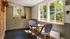 Et værelse med spisebord, stole, et vindue med udsigt til grønne områder, en radiator og en vægmonteret lampe.