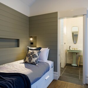 Un dormitorio moderno con cama, mesita de noche, luz de pared y baño con lavamanos y espejo.