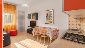 A compact kitchen with a gas stove, a dining table with chairs, a TV, and a framed artwork on the wall. - Ca di Valle Retreats (Cavallino-Treporti)
