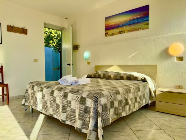Ein Schlafzimmer mit einem Bett, einem Sessel, einem Nachttisch, einem Bild und einer Tür, die nach draußen führt.