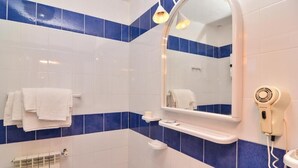 Ein Badezimmer mit weißen und blauen Fliesen, einem Waschbecken, einem Spiegel, einem Handtuchhalter und einem Fön.